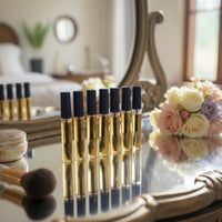 A series of small bottles with a golden yellow liquid and applicator wand inside, displayed on a table with a soft focused background.