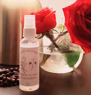 Picture shares a picture of the Emisha Wellness Rose Water in a 60ml size. This particular one is set with the backdrop of life with two beautiful & vibrant red roses next to Tiger's Eye crystals resting close by. The Rose and Geranium Water is also restfully present while gently announcing its soft presence with